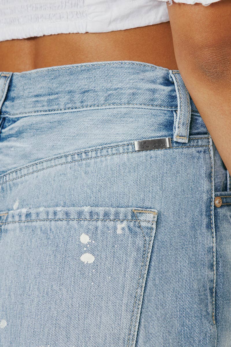 pocket detail of High Rise Slim Straight Jeans in Medium Stone Wash, featuring a 12" rise, 28" inseam, rigid 100% cotton fabric, frayed hem, paint splatter accents, and distressed details with a zip fly.
