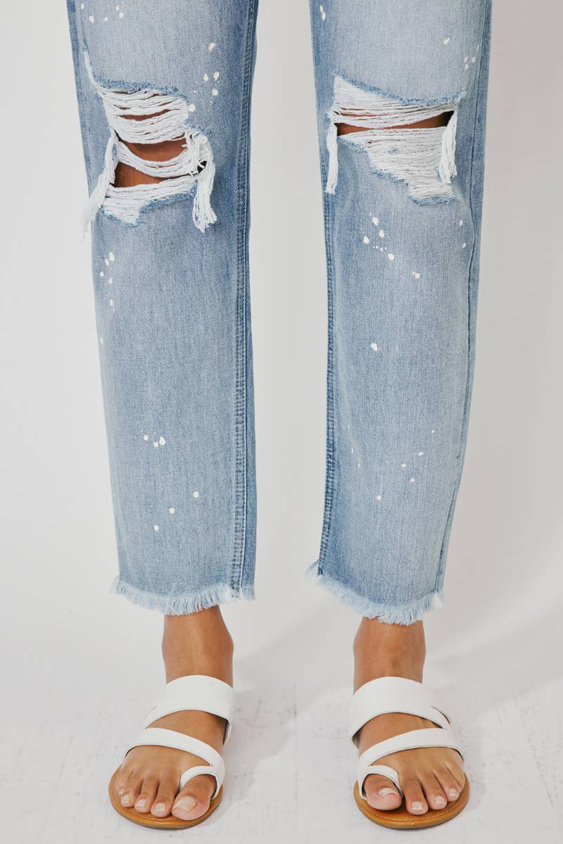 detail of distressed parts of High Rise Slim Straight Jeans in Medium Stone Wash, featuring a 12" rise, 28" inseam, rigid 100% cotton fabric, frayed hem, paint splatter accents, and distressed details with a zip fly.