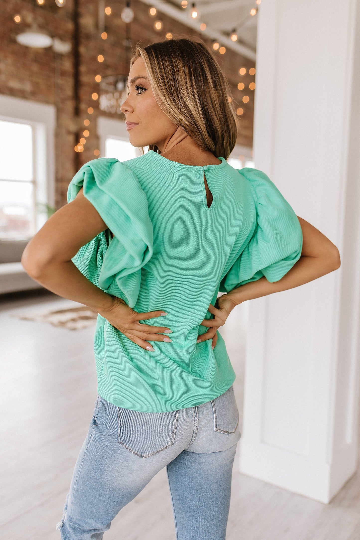 back view of Aurelia blouse featuring delicate ruffle sleeves, made from 65% cotton, 33% polyester, and 2% elastane, offering an elegant and comfortable look.