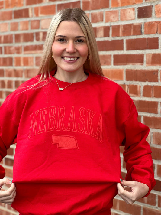 Unisex red crew sweatshirt with State of Nebraska design in red puff ink, made from a comfortable 50/50 cotton-poly blend.