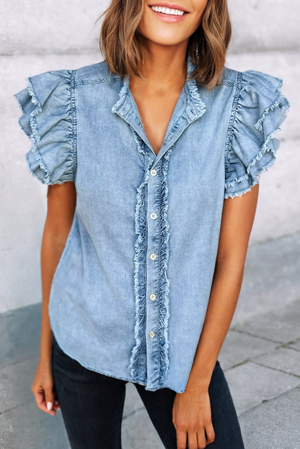 Button front denim blouse with ruffle and flutter sleeves, featuring a frayed hem for a casual and chic look.